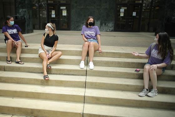 四名冰球突破app学生的照片，戴着面具，坐在图书馆的台阶上